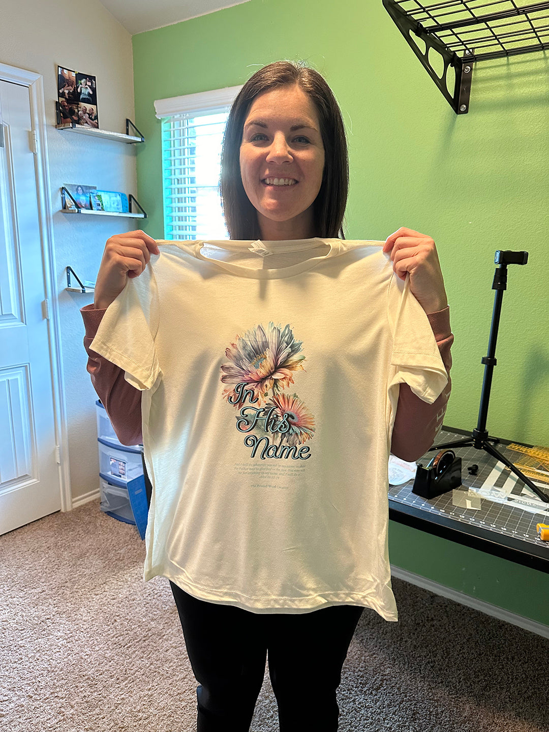 Nicole holding an earlier cream In His Name tee in the studio
