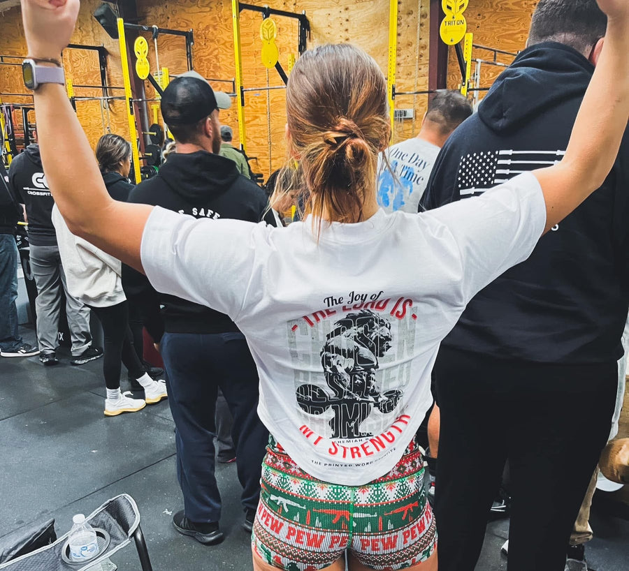 Woman at a gym event in The Joy of the Lord tee, arms up